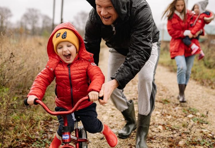 Father helping son ride a bicycle on a fall day while mother and daughter watch.