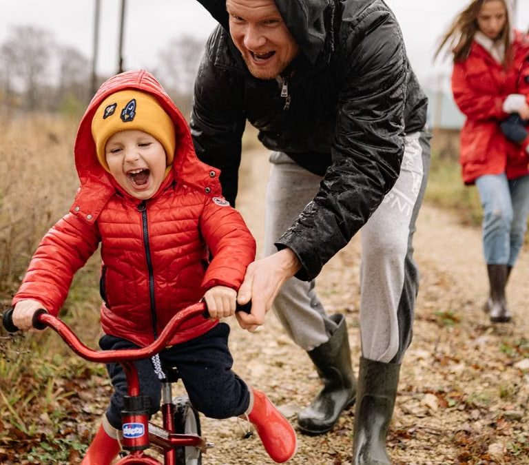 Father helping son ride a bicycle on a fall day while mother and daughter watch.