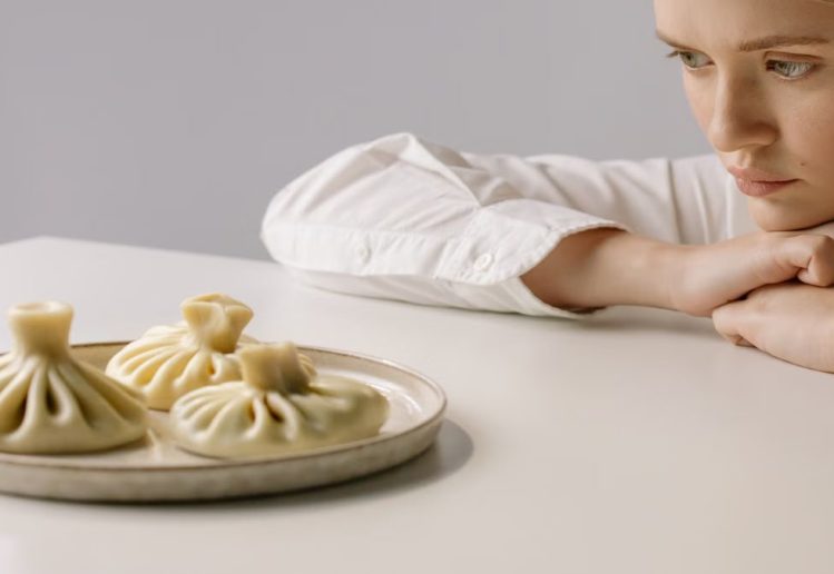A woman in a white shirt gazes at a plate of traditional Georgian khinkali dumplings.