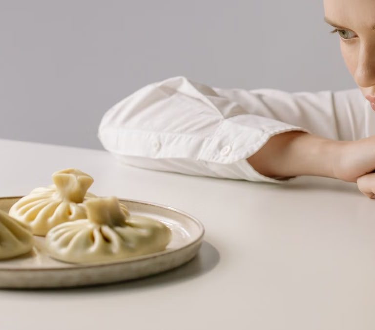 A woman in a white shirt gazes at a plate of traditional Georgian khinkali dumplings.