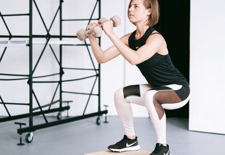 A woman in sportswear performs a squat with dumbbells indoors, embodying strength and healthy living.